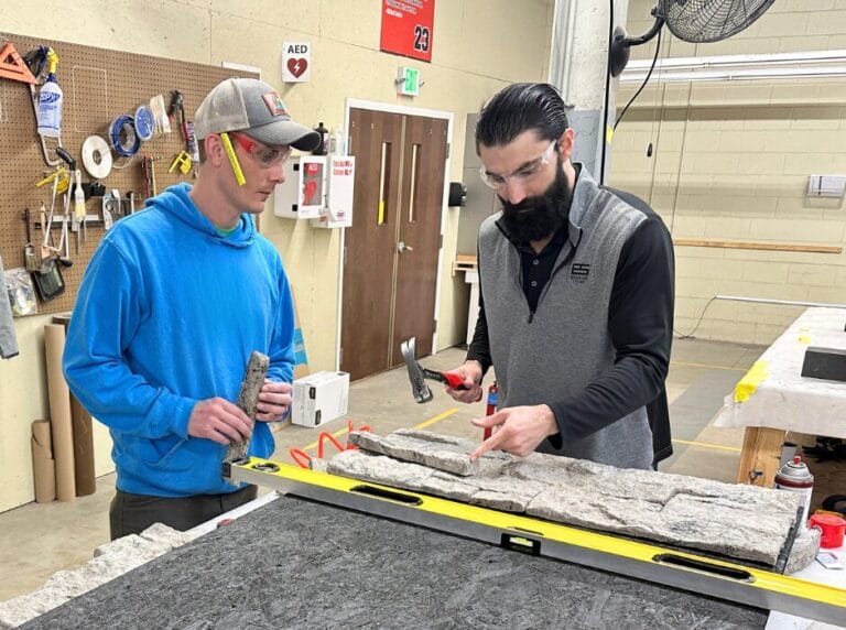 Daniel Fritz, VP for Evolve Stone (right), shows Douglas Hicks of ActivWall (left) tips for installing Evolve Stone mortarless, nailable stone veneer on a wall panel for ActivWall's booth at The International Builders' Show.